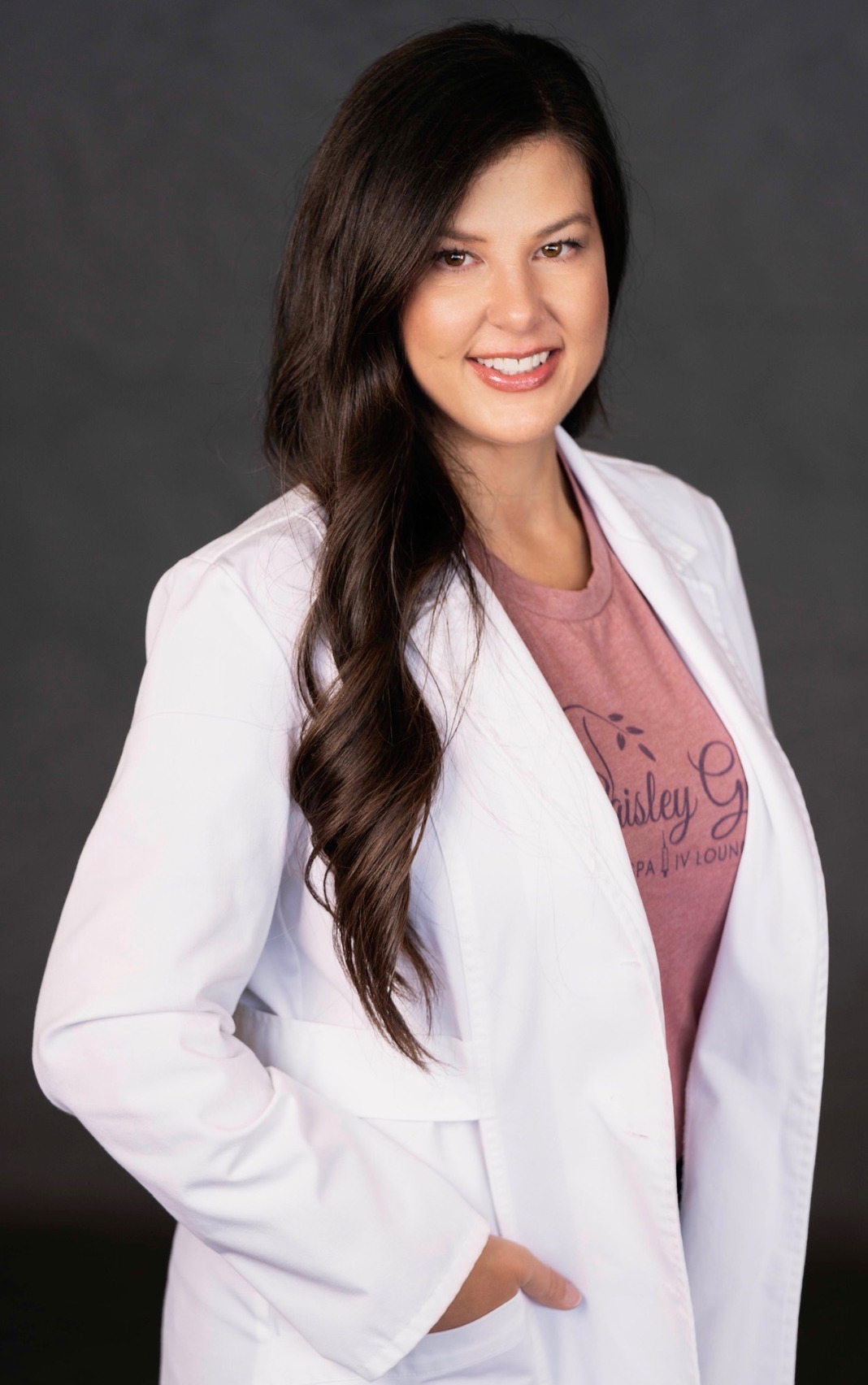 A woman with long black hair, pink shirt and white lab coat.
